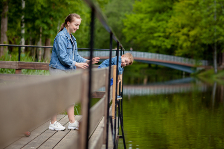 Mother is experiencing that the child will fall into the water. A little boy climbs a bridge railing in the park. The threat of drowning. Danger to children.の写真素材