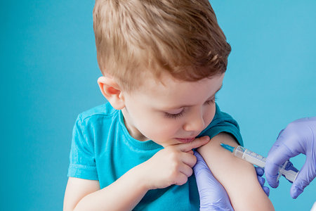 Vaccination concept. Female doctor vaccinating cute little boy on blue background, closeup.