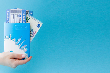Passport, euro and air ticket in woman hand on a blue background. Travel concept, copy space.