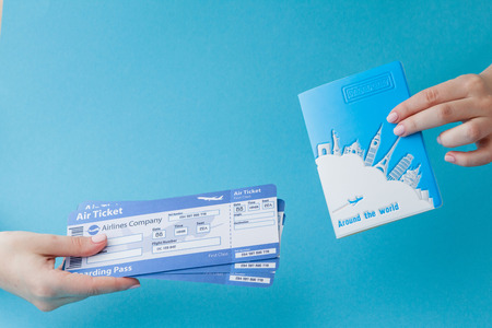 Passport and air ticket in woman hand on a blue background. Travel concept, copy space.の写真素材