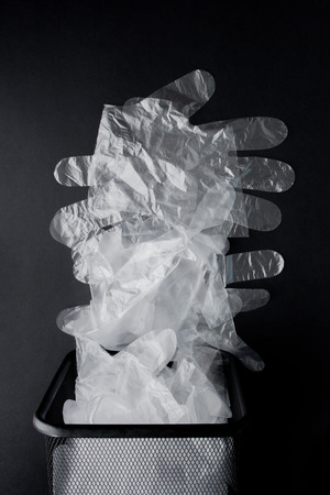 Plastic bag with handles, gloves in the bin on a black background . Used plastic bag for recycling. Concept - ecology, planet pollution with plastic cellophane polyethylene.の写真素材