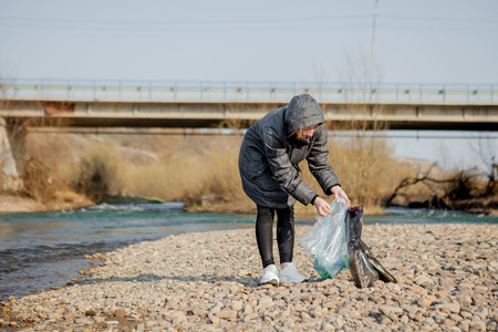 Young woman collecting plastic trash from the beach and putting it into black plastic bags for recycle. Cleaning and recycling conceptの写真素材