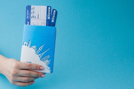 Passport and air ticket in woman hand on a blue background. Travel concept, copy space.の写真素材