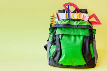 Composition with backpack and school stationery on yellow background.