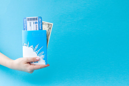 Passport, dollars and air ticket in woman hand on a blue background. Travel concept, copy space