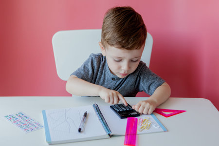 Portrait of cute kid boy at home making homework. Little concentrated child writing with colorful...