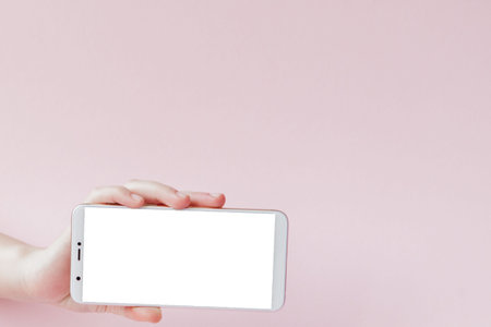 Modern mobile phone in a woman's hand on pink background.