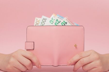 Pink purse and Euro banknotes in Female hands on pink background. Business Conceptの写真素材