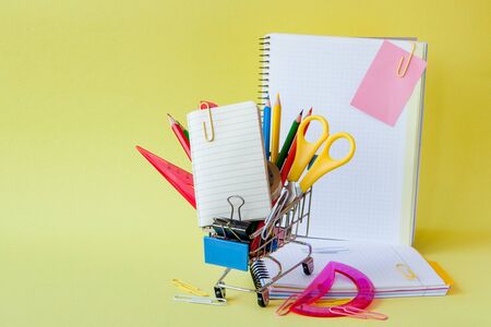 Shopping cart with different stationery on the yellow background.の写真素材