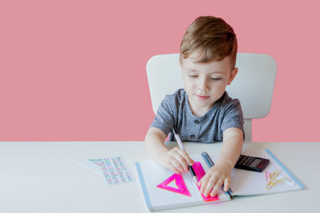 Portrait of cute kid boy at home making homework. Little concentrated child writing with colorful...