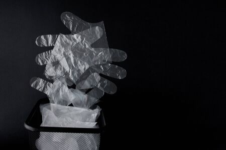 Plastic bag with handles, gloves in the bin on a black background . Used plastic bag for recycling. Concept - ecology, planet pollution with plastic cellophane polyethylene.の写真素材