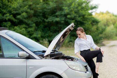 Young woman by the roadside after her car has broken down She opened the hood to see the damage.の写真素材