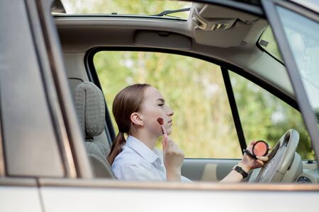 Picture of young businesswoman doing makeup while driving a car in the traffic jam.の写真素材