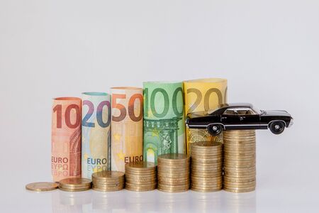 A black model of a car and ten, twenty, fifty, one hundred, two hundred and coins euro rolled bills banknotes on white background. Histogram from the euro. Concept of currency growth, savingsの写真素材