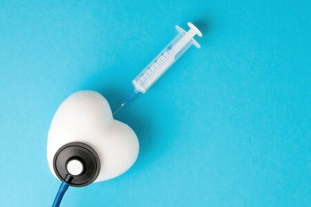 White Heart Shape with a Syringe on the Blue Paper Background closeup.Top view.Copy spaceの写真素材