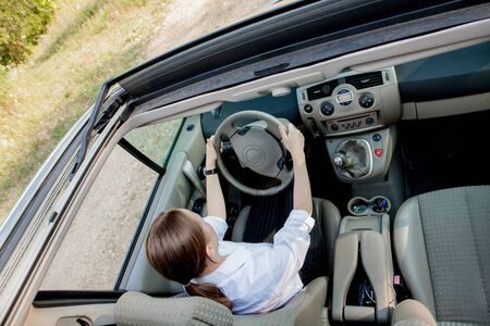Close up portrait of pleasant looking female with glad positive expression, being satisfied with unforgettable journey by car, sits on driver s seat. People, driving, transport concept.の写真素材