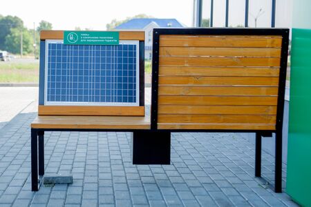 Outdoor shot of wooden bench in park having solar power panel installed, USB cable connected to smartphone.の写真素材