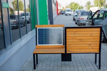 Outdoor shot of wooden bench in park having solar power panel installed, USB cabel connected to smartphone.の写真素材