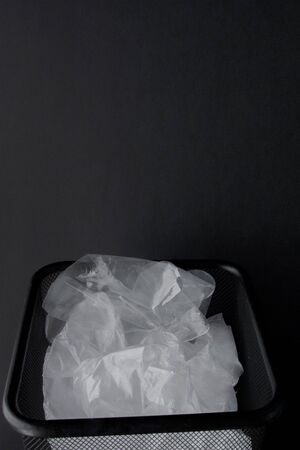 Plastic bag with handles, gloves in the bin on a black background . Used plastic bag for recycling. Concept - ecology, planet pollution with plastic cellophane polyethylene.の写真素材