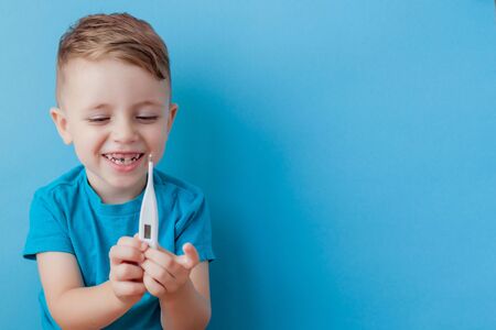 Ill young child with a thermomether, measuring the height of his fever and looking into the camera.の写真素材