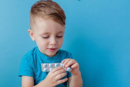 A small child holds in his palm a handful of pills on blue backgroundの写真素材