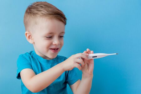 Ill young child with a thermomether, measuring the height of his fever and looking into the camera.の写真素材