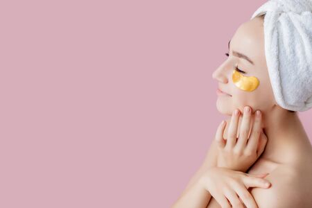Portrait of Beauty Woman with Eye Patches on pink background. Woman Beauty Face with Mask under Eyes. Beautiful Female with natural Makeup and Gold Cosmetics Collagen Patches on Fresh Facial Skin.の写真素材