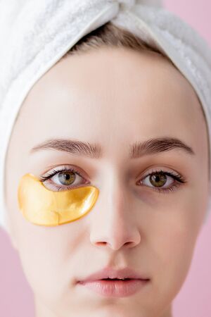 Portrait of Beauty Woman with Eye Patches on pink background. Woman Beauty Face with Mask under Eyes. Beautiful Female with natural Makeup and Gold Cosmetics Collagen Patches on Fresh Facial Skin.の写真素材