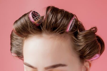Beautiful girl in hair curlers on pink background.の写真素材
