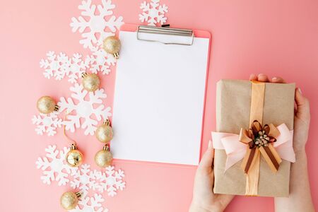 Christmas gift in women's hands and notebook on a pink background, a view from above.の写真素材