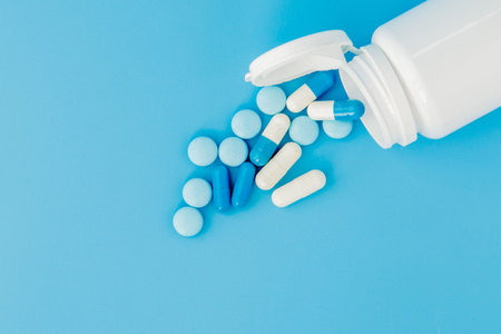 Assorted pharmaceutical medicine pills, tablets and capsules and bottle on blue background. Copy...