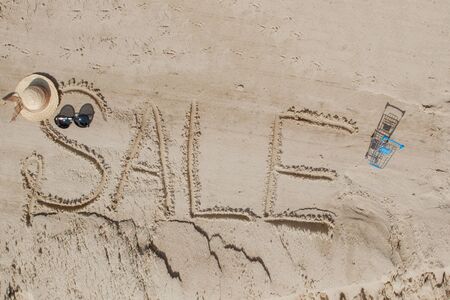 The word sale is painted on the sand. Beach background. View from above. The concept of summer, summer kanikkuly, vacation, holydaysの写真素材