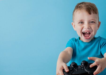 Little kid boy 2-3 years old wearing blue clothes hold in hand joystick for gameson blue background children studio portrait. People childhood lifestyle concept. Mock up copy space.の写真素材
