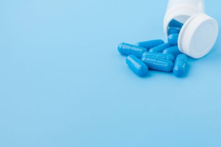 Blue capsules, pills on a blue background. Capsules in a white jar. Vitamins, nutritional supplements for women's health.の写真素材