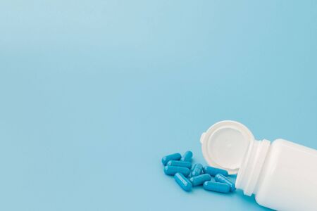 Blue capsules, pills on a blue background. Capsules in a white jar. Vitamins, nutritional supplements for women's health.の写真素材