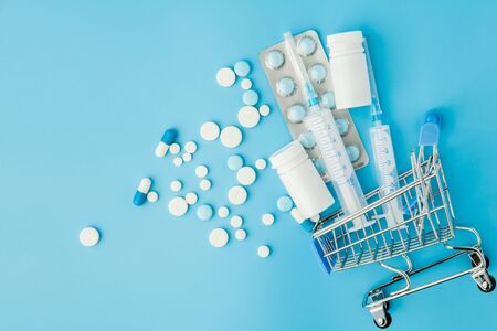 Pills and medical injection in shopping trolley on blue background. Creative idea for health care cost, drugstore, health insurance and pharmaceutical company business concept. Copy spaceの写真素材