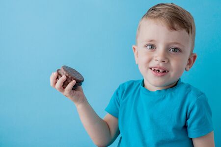 Portrait of confident attractive little boy holds american chocolate chip cookies on blue background.の写真素材