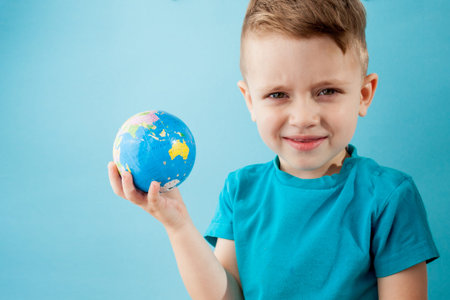 Little boy holding a globe on blue background.の写真素材