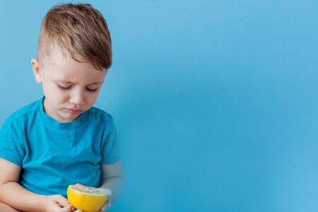 Little, blond boy biting into a lemon and make a face.の写真素材