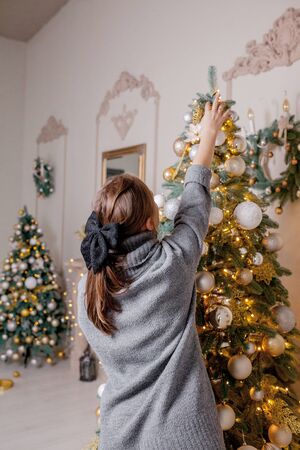 x-mas, winter holidays and people concept - happy young woman decorating christmas tree at home.の写真素材