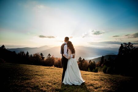 Bride and groom watch the sunset standing on the hill.の写真素材