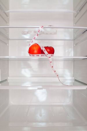 Empty refrigerator with a persimmon and green apple and tape measuring on the shelf, diet concept, blurred background.の写真素材