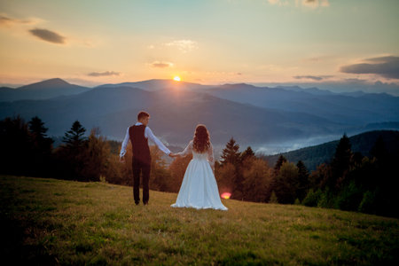Bride and groom watch the sunset standing on the hill.