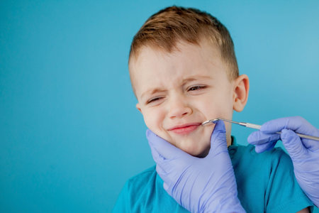 Small patient does not want to open the dentist's mouth on blue background. Dantist treats teeth. close up view of dentist treating teeth of little boy in dentist officeの写真素材