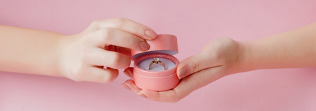 Woman opens a gift box with jewellery. Wedding ring in a box in the hands of women on a pink...