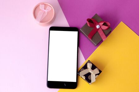Phone screen and gifts on colored background. Minimal concept. Flat lay. top view.Online promotions and discounts. Holiday gifts and surprises. Present. Valentine's Day. Internet technologies.の写真素材