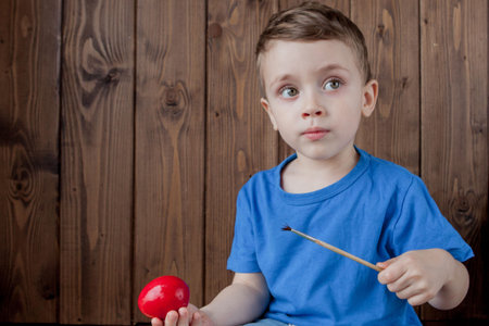 Happy baby boy with a basket of easter eggs on wooden background.