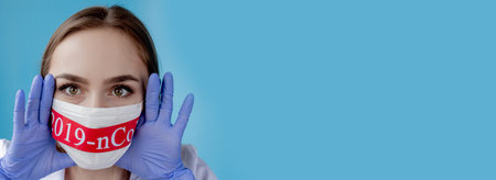 Doctor woman with surgical mask pointing to red paper with mesaage Coronavirus on blue background....