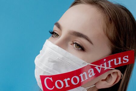 Doctor woman with surgical mask pointing to red paper with mesaage Coronavirus on blue background. World Health Organization WHO introduced new official name for Coronavirus disease named COVID-19.の写真素材