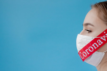 Doctor woman with surgical mask pointing to red paper with mesaage Coronavirus on blue background....